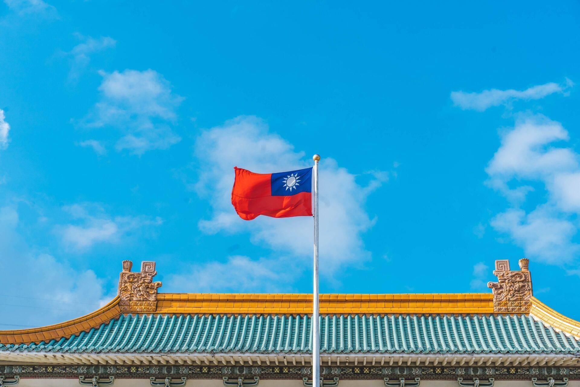 Le drapeau de Taïwan flottant devant un temple traditionnel aux toits dorés et turquoise sous un ciel bleu