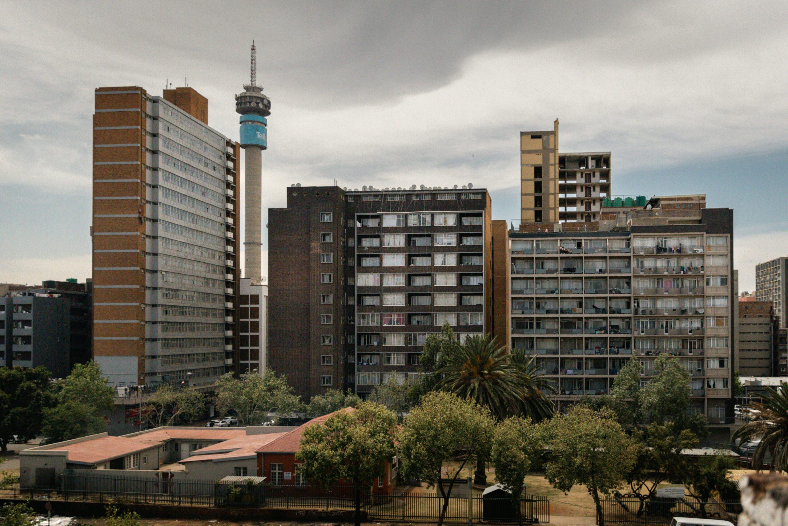 Skyline urbain avec immeuble de brique rouge, tour de télécommunications bleue et bâtiments résidentiels sous ciel nuageux