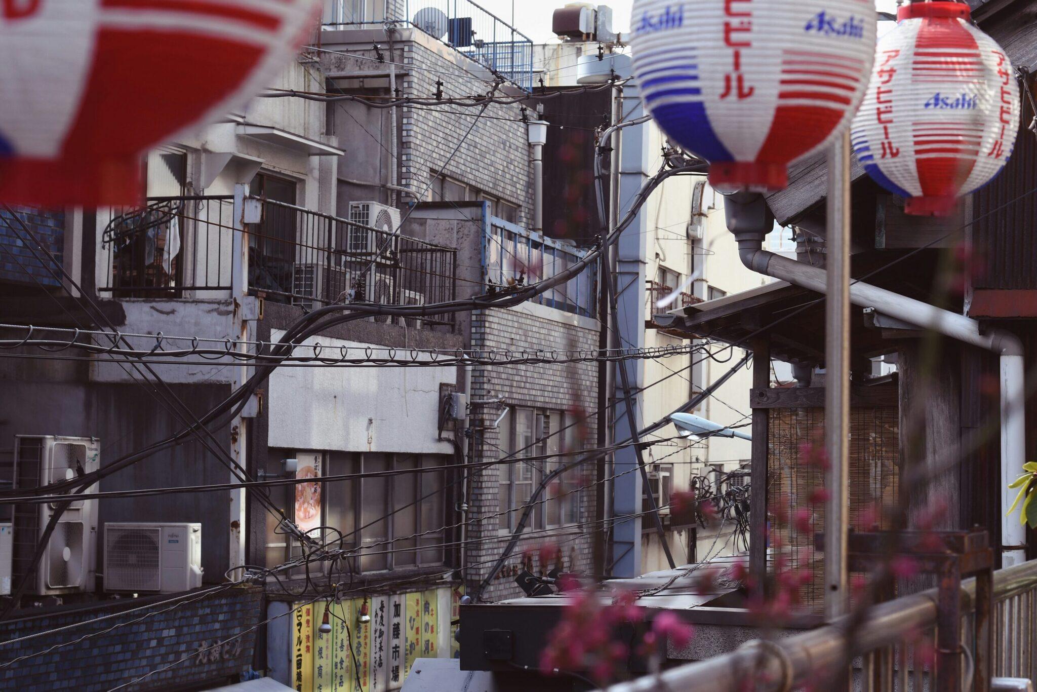 Une ruelle japonaise typique avec lanternes rouges et bleues Asahi, fils électriques enchevêtrés et petits bâtiments résidentiels traditionnels