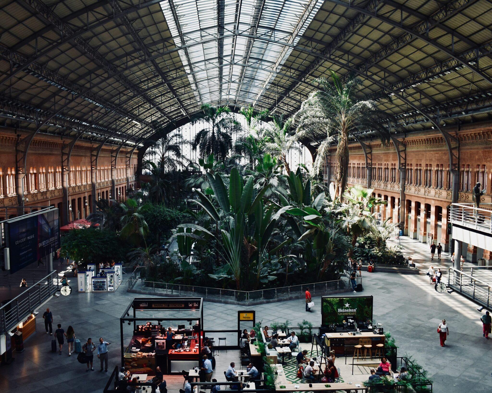 Vue aérienne d’une gare historique rénovée avec verrière métallique, jungle intérieure et restaurants, architecture victorienn rouge brique