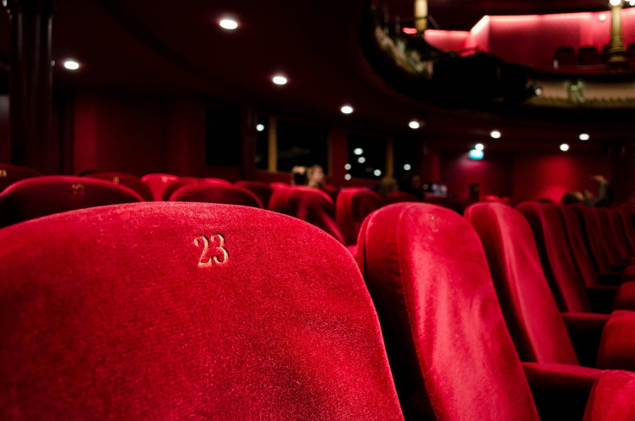 Rangée de fauteuils rouges numérotés dans une salle de cinéma élégante, siège 23 en premier plan