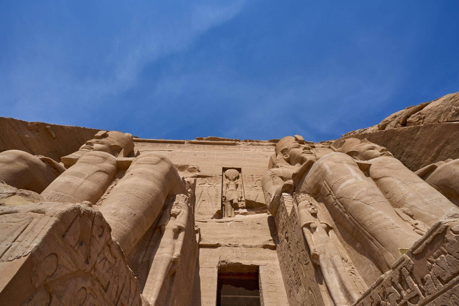 Façade monumentale d’un temple égyptien antique avec colosses sculptés et hiéroglyphes sous ciel bleu