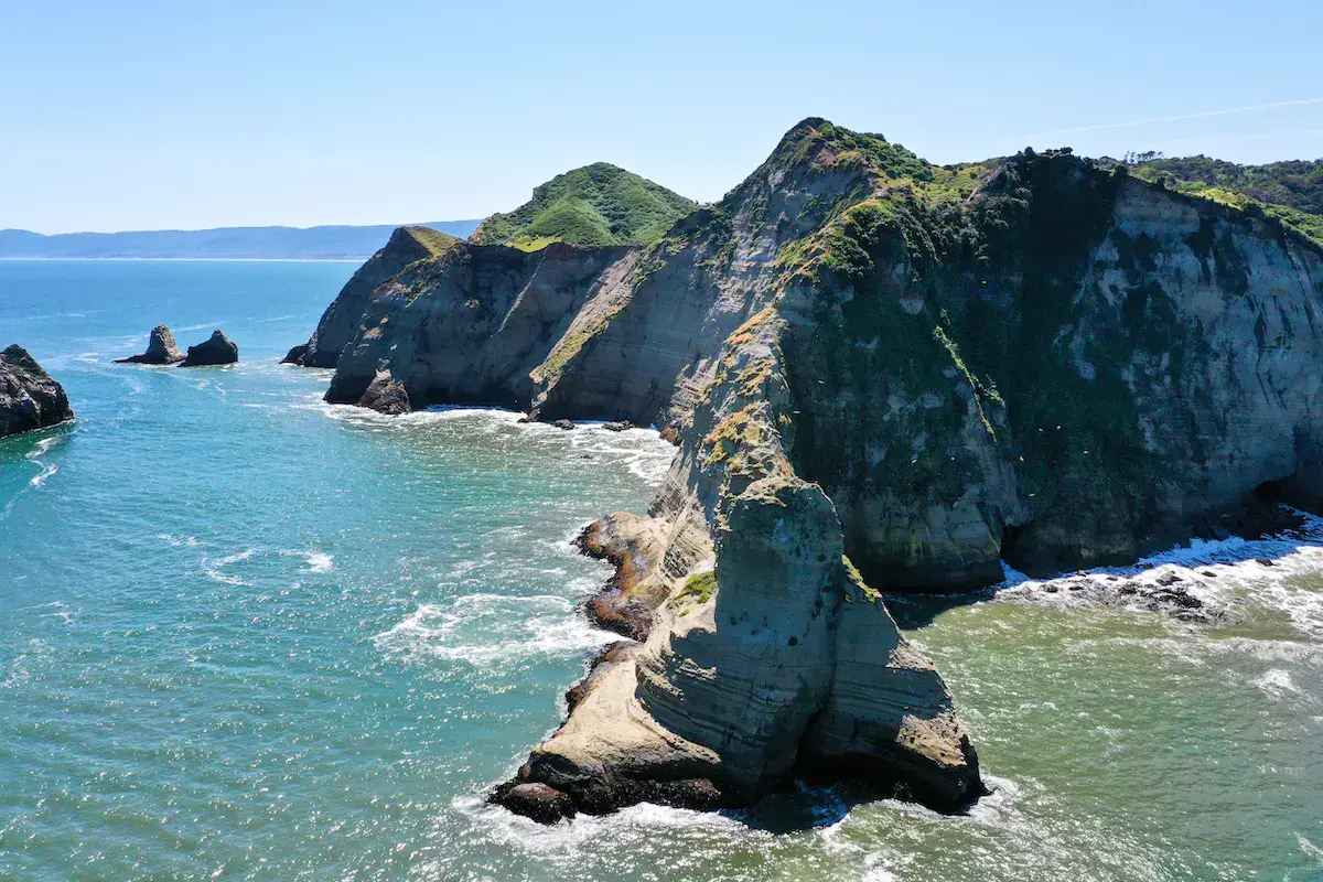 Falaises rocheuses verdoyantes surplombant l’océan turquoise avec formations géologiques spectaculaires et îlots en arrière-plan