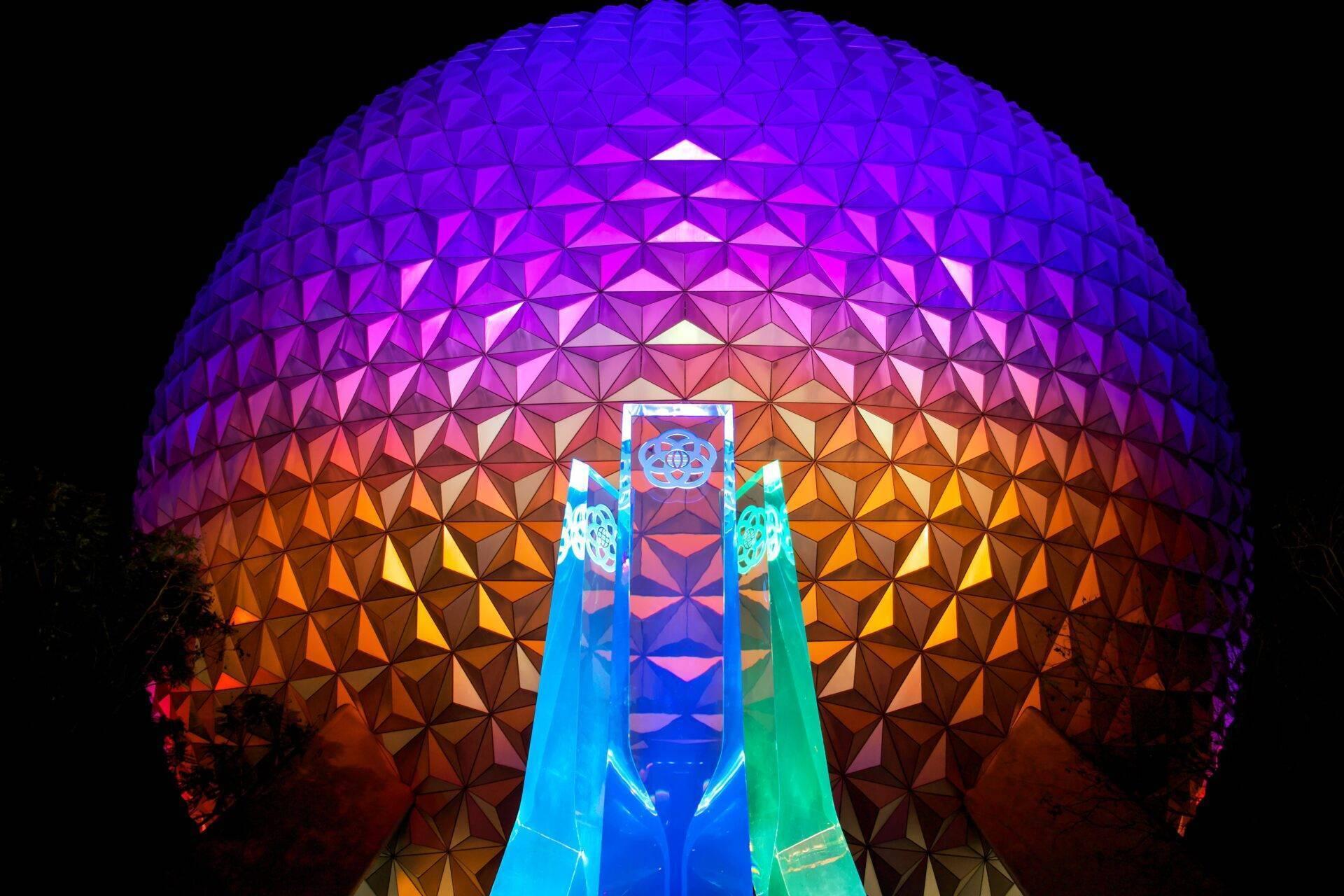 Une structure géodésique sphérique illuminée la nuit en dégradé de couleurs, avec une entrée monumentale bleue et verte