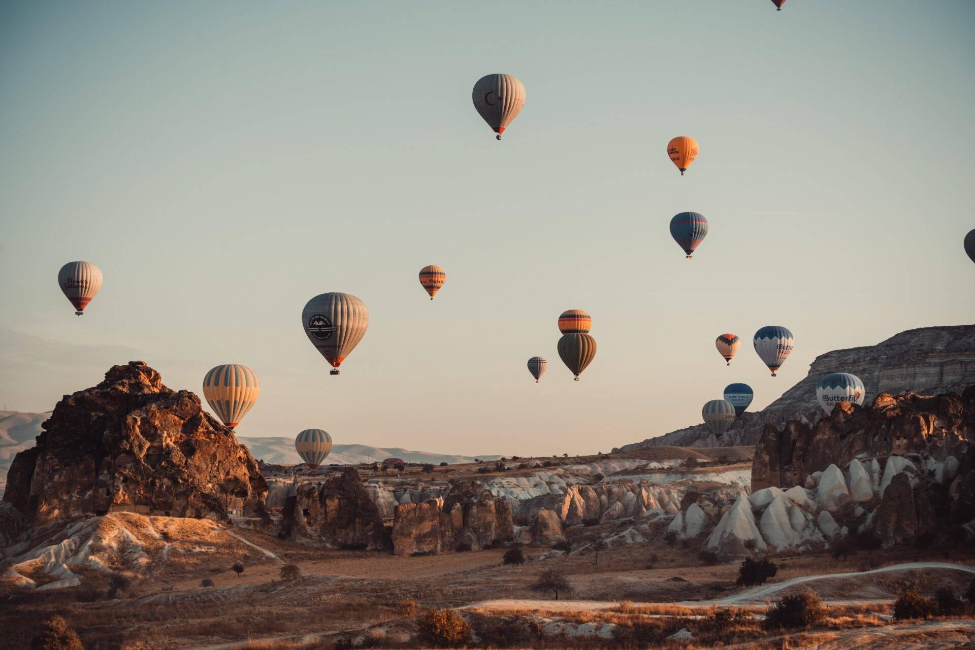 Plusieurs montgolfières colorées survolent des formations rocheuses en pierre blanche au lever du soleil