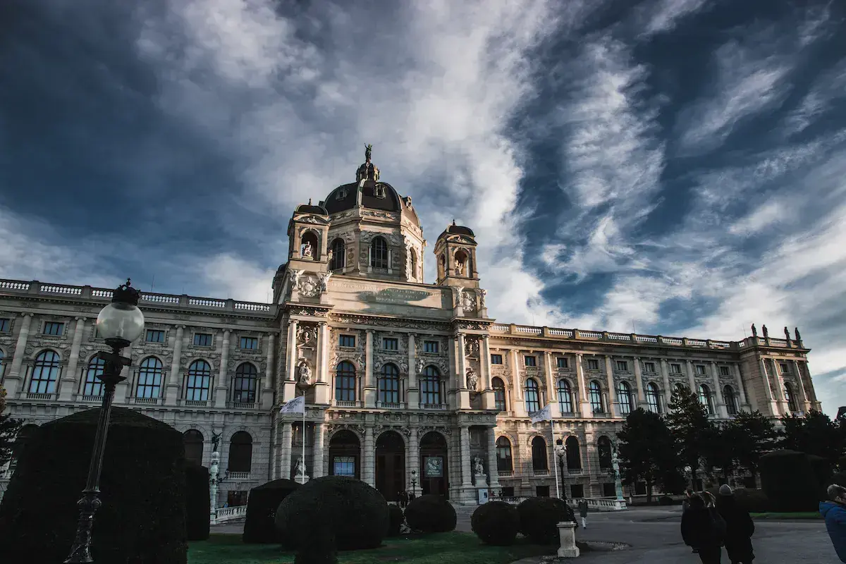 Un imposant bâtiment baroque blanc avec dômes dorés sous un ciel nuageux dramatique