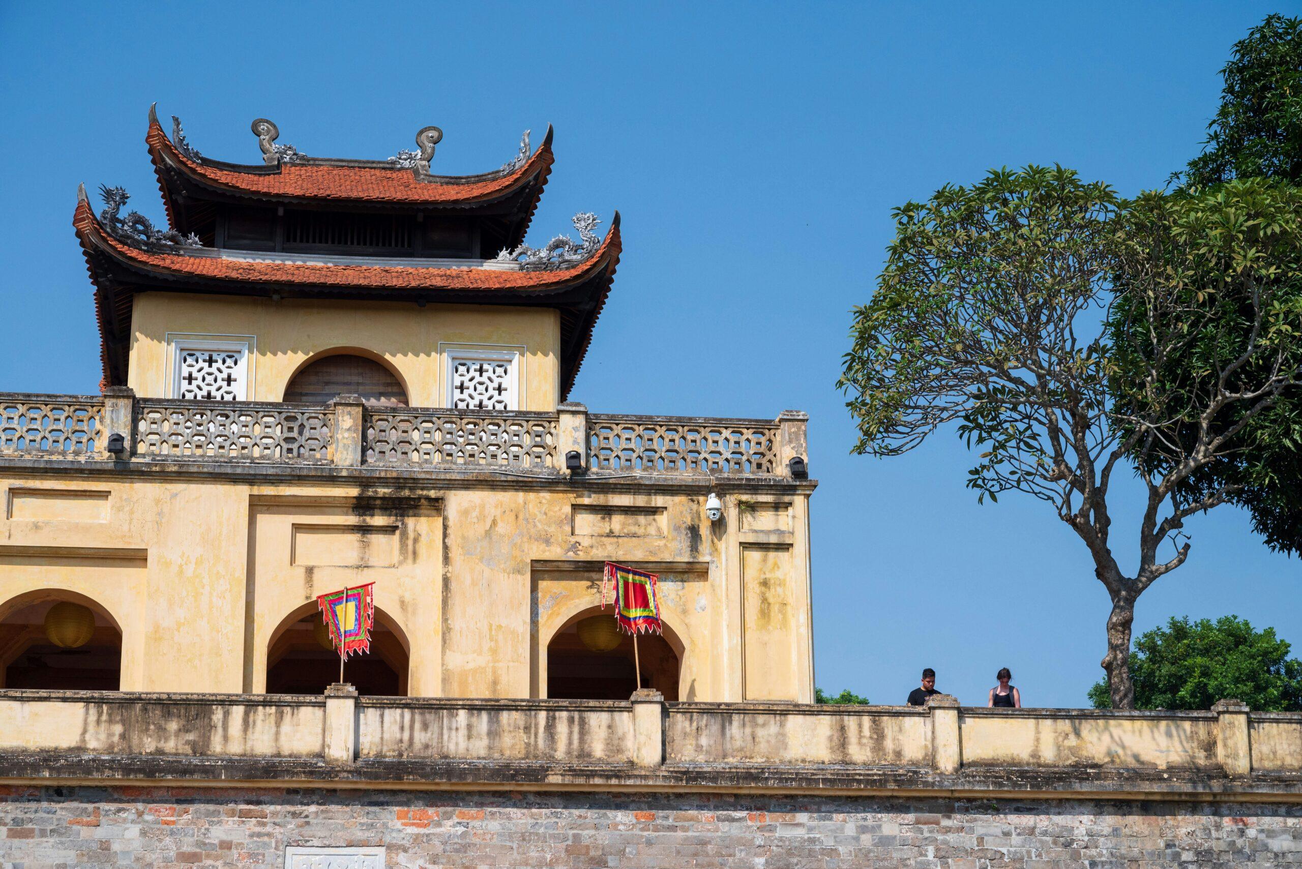 Temple asiatique aux toits recourbés rouges et murs jaunes avec balcon fleuri sous ciel bleu