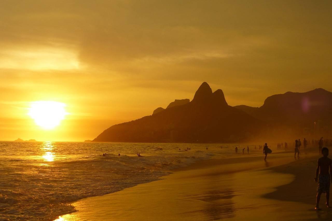 Coucher de soleil doré sur une plage brésilienne avec montagne rocheuse et baigneurs