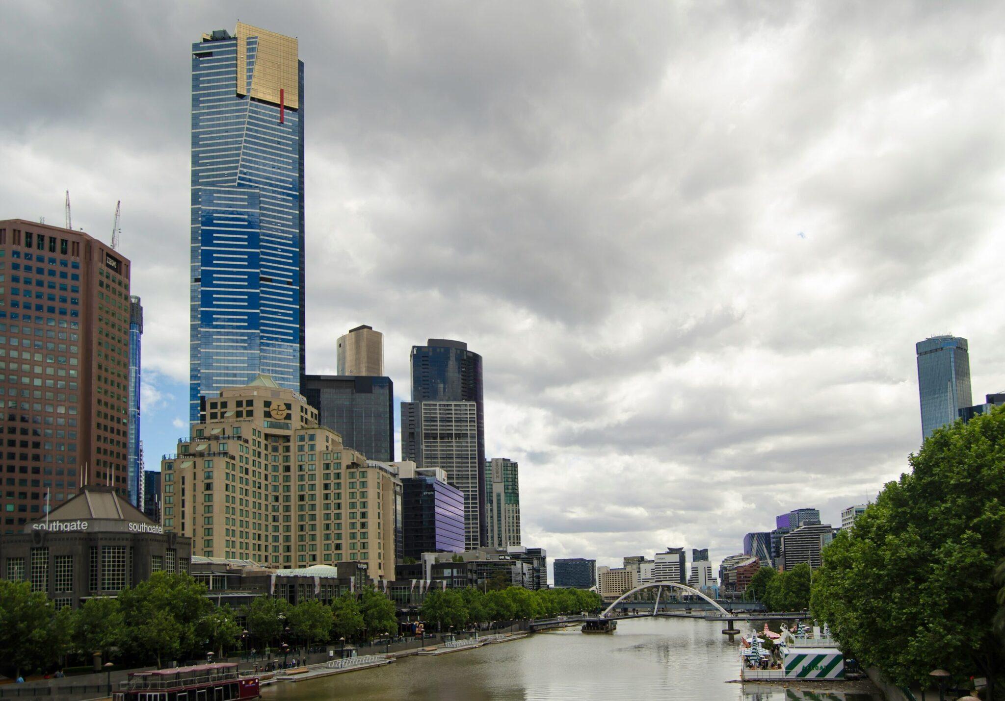Skyline urbain avec gratte-ciel modernes, rivière et pont arqué, arbres verdoyants, ciel nuageux