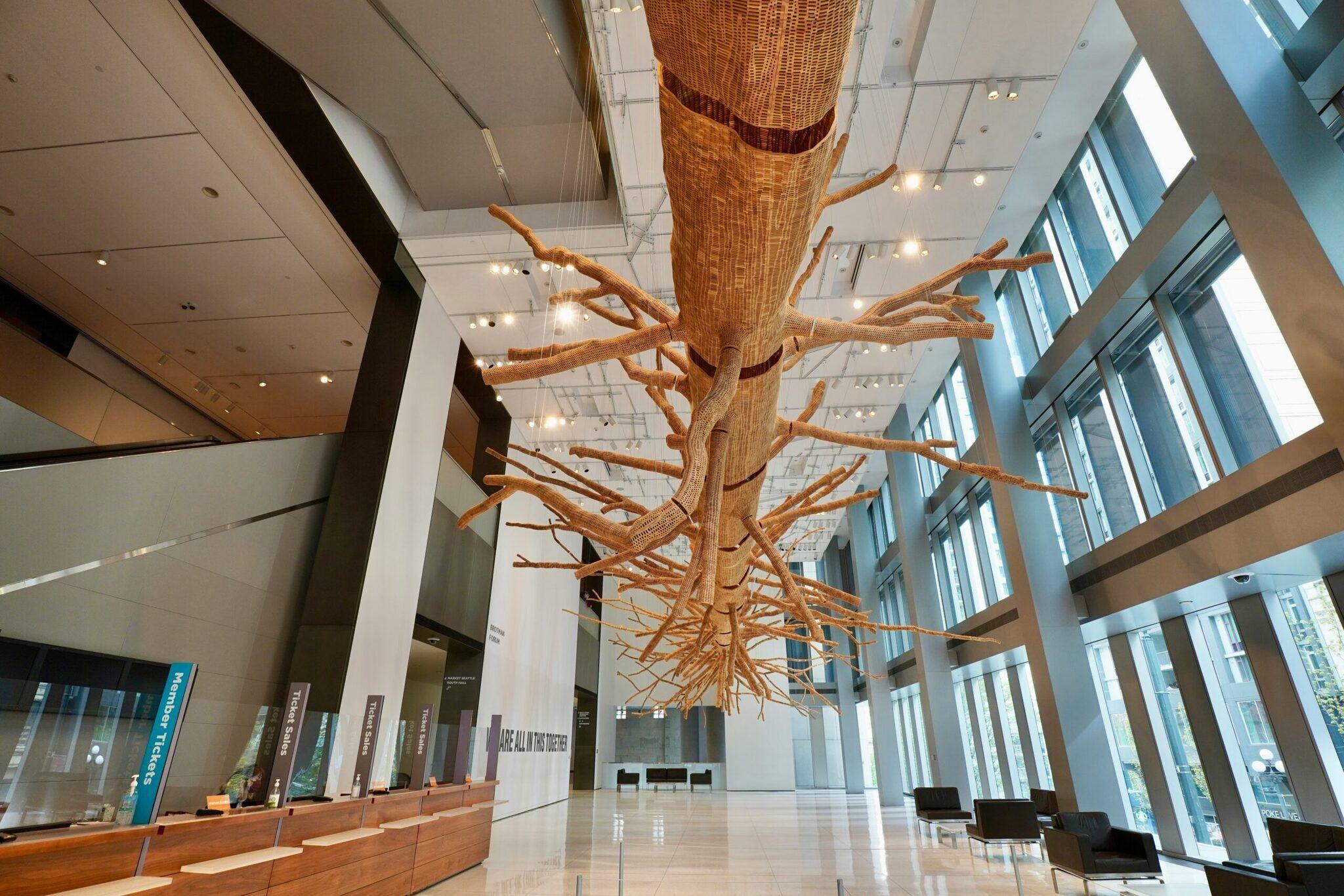 Une installation artistique en bois représentant un arbre géant suspendu au plafond d’un hall moderne lumineux