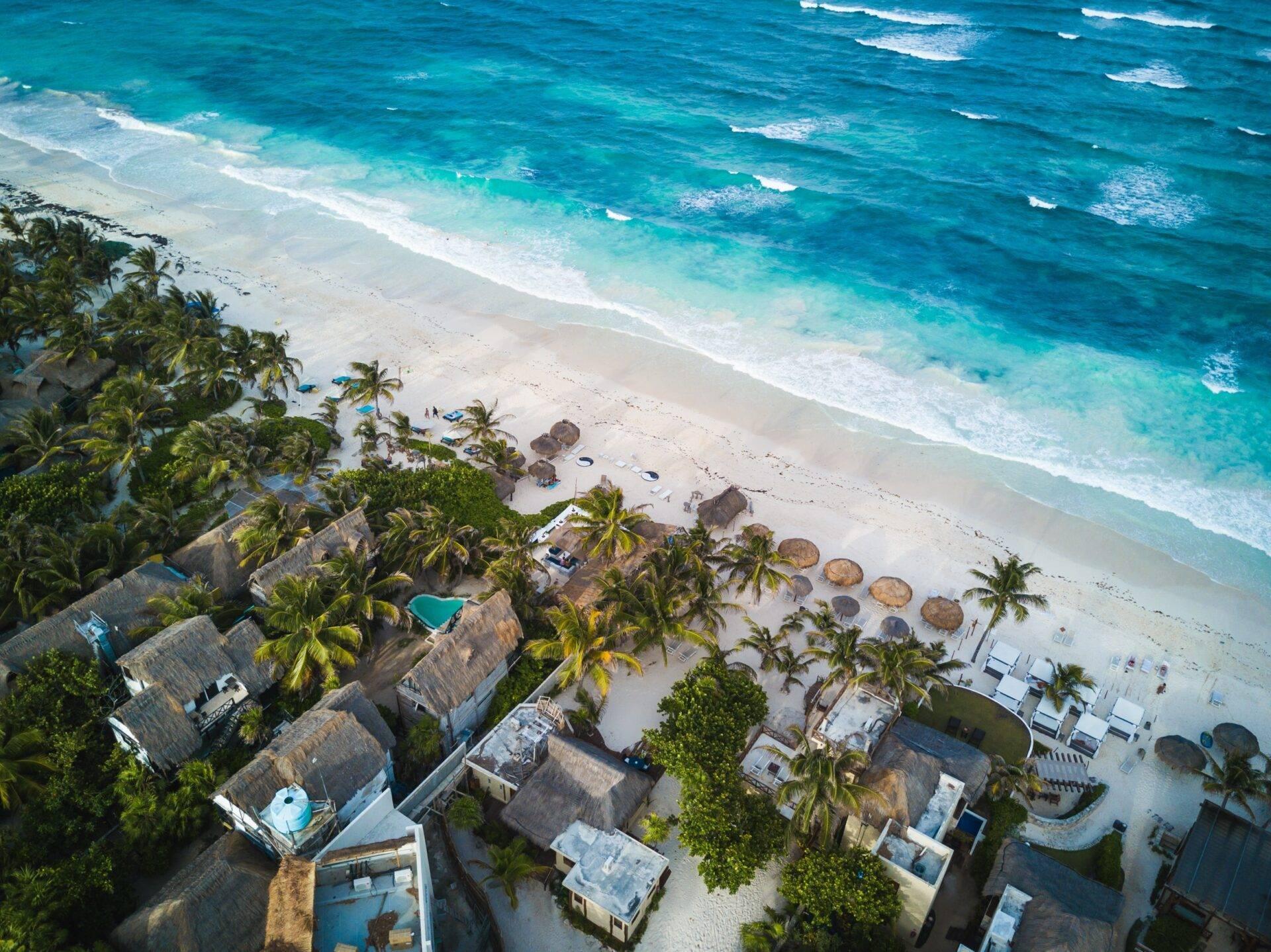 Vue aérienne d’une plage de sable blanc avec resort tropical, palmiers et eaux turquoise