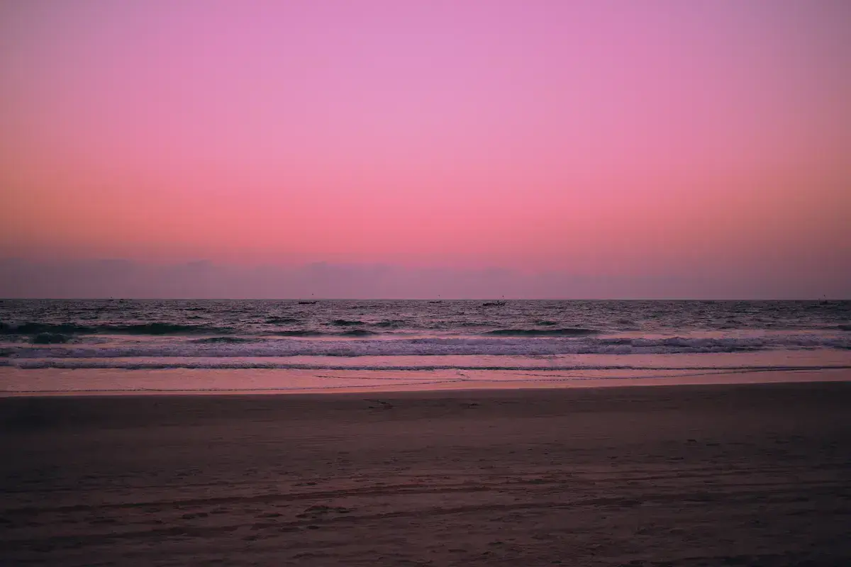 Coucher ou lever de soleil rose sur une plage déserte avec vagues déferlantes et ciel dégradé