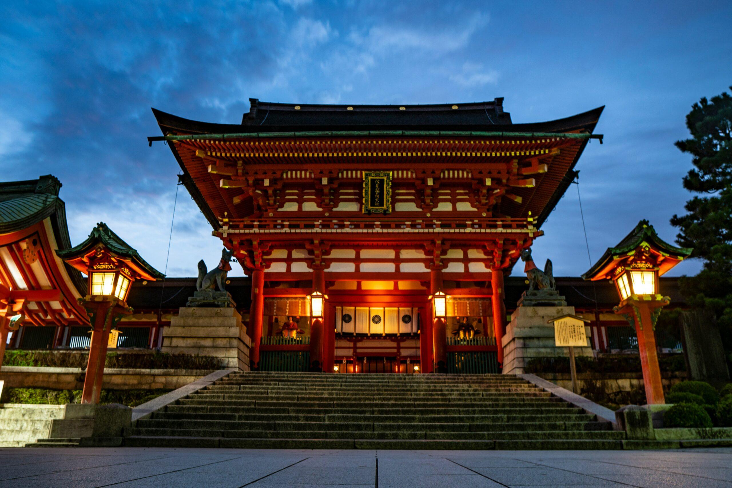 Un temple japonais illuminé au crépuscule avec portes rouges vermillon, lanternes dorées et escalier monumental