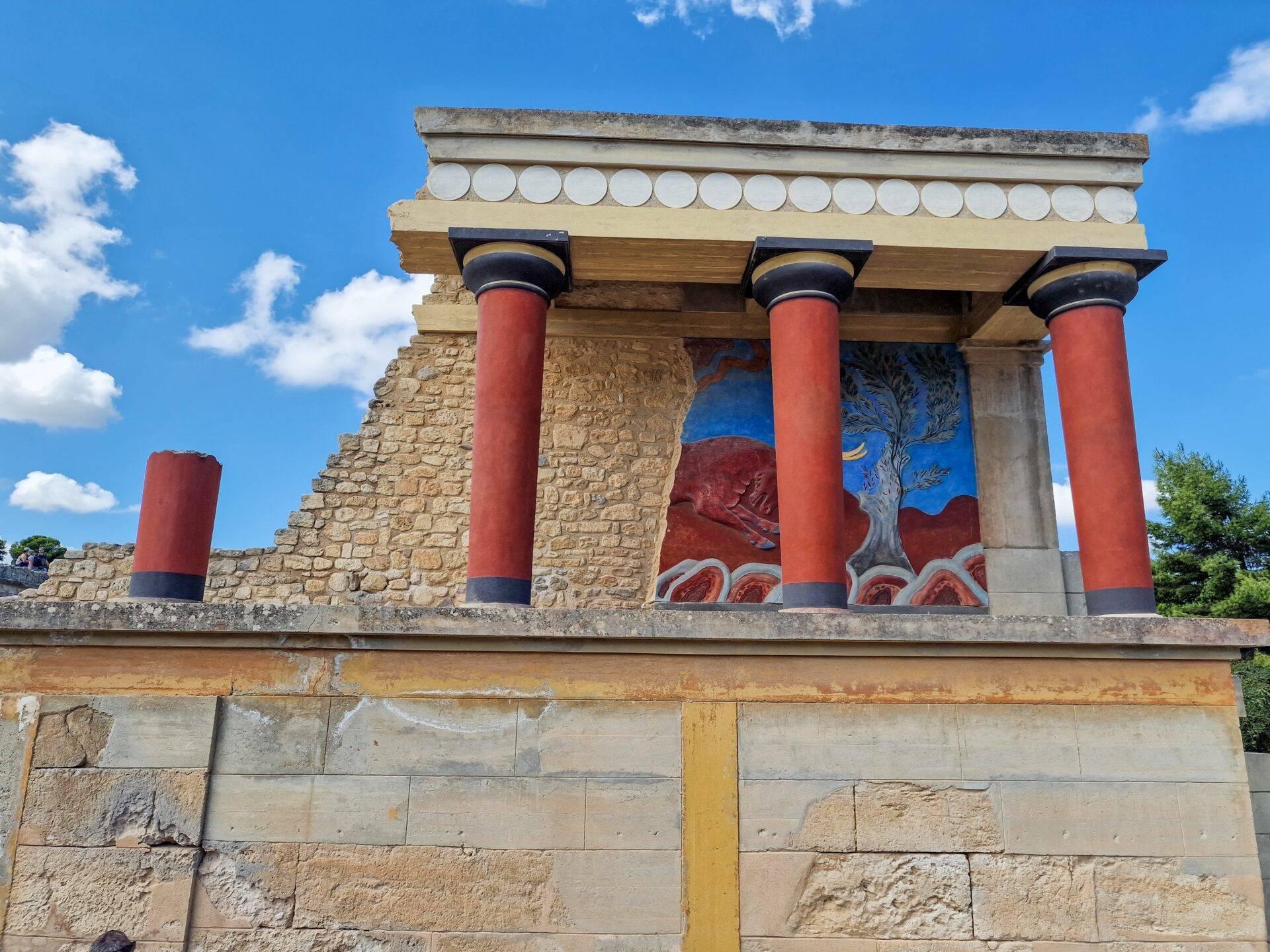 Reconstitution d’un temple minoen avec colonnes rouge vif et fresques décoratives sous un ciel bleu dégagé