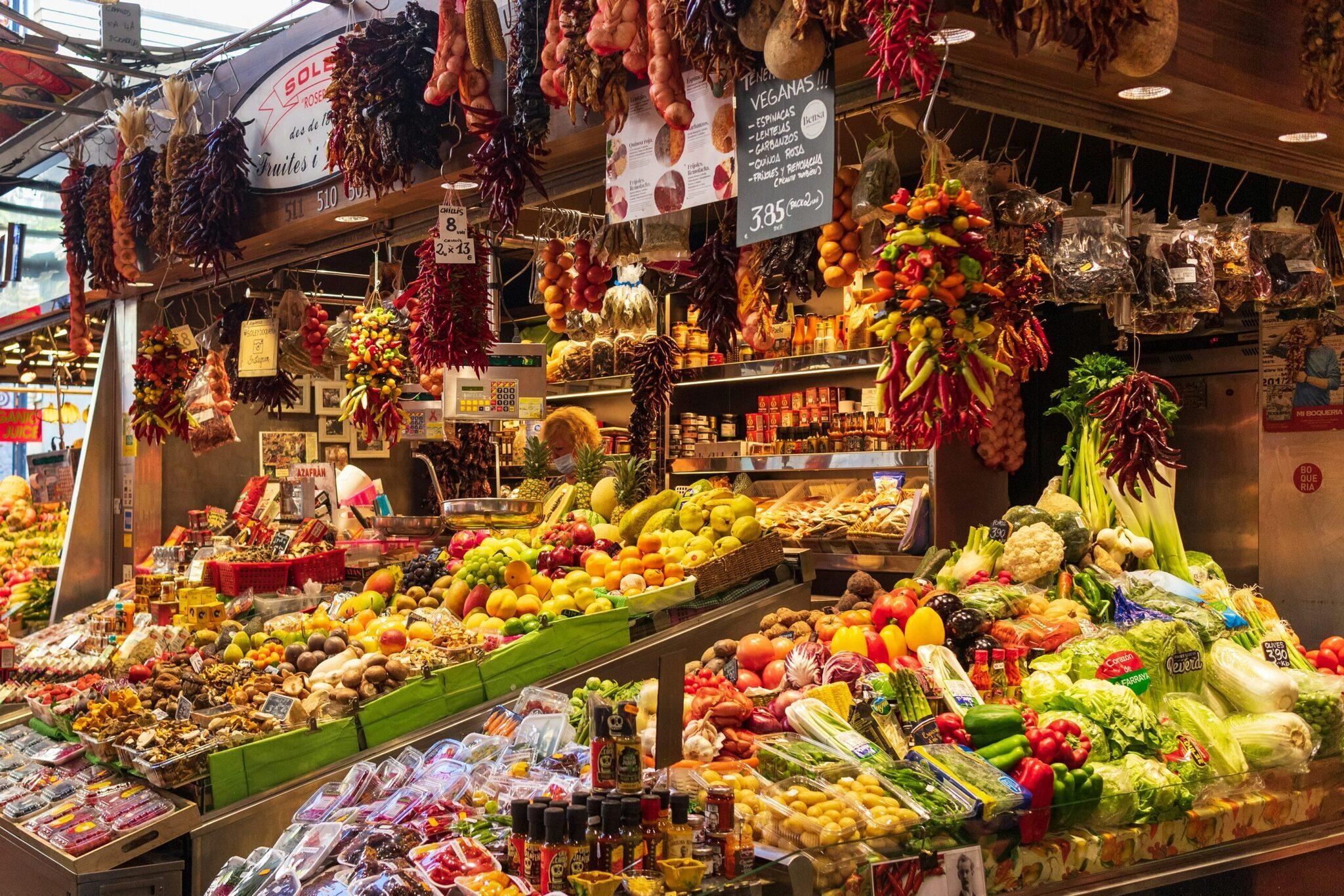 Un étal de marché couvert débordant de fruits, légumes frais et produits locaux suspendus, illustrant la richesse gastronomique méditerranéenne