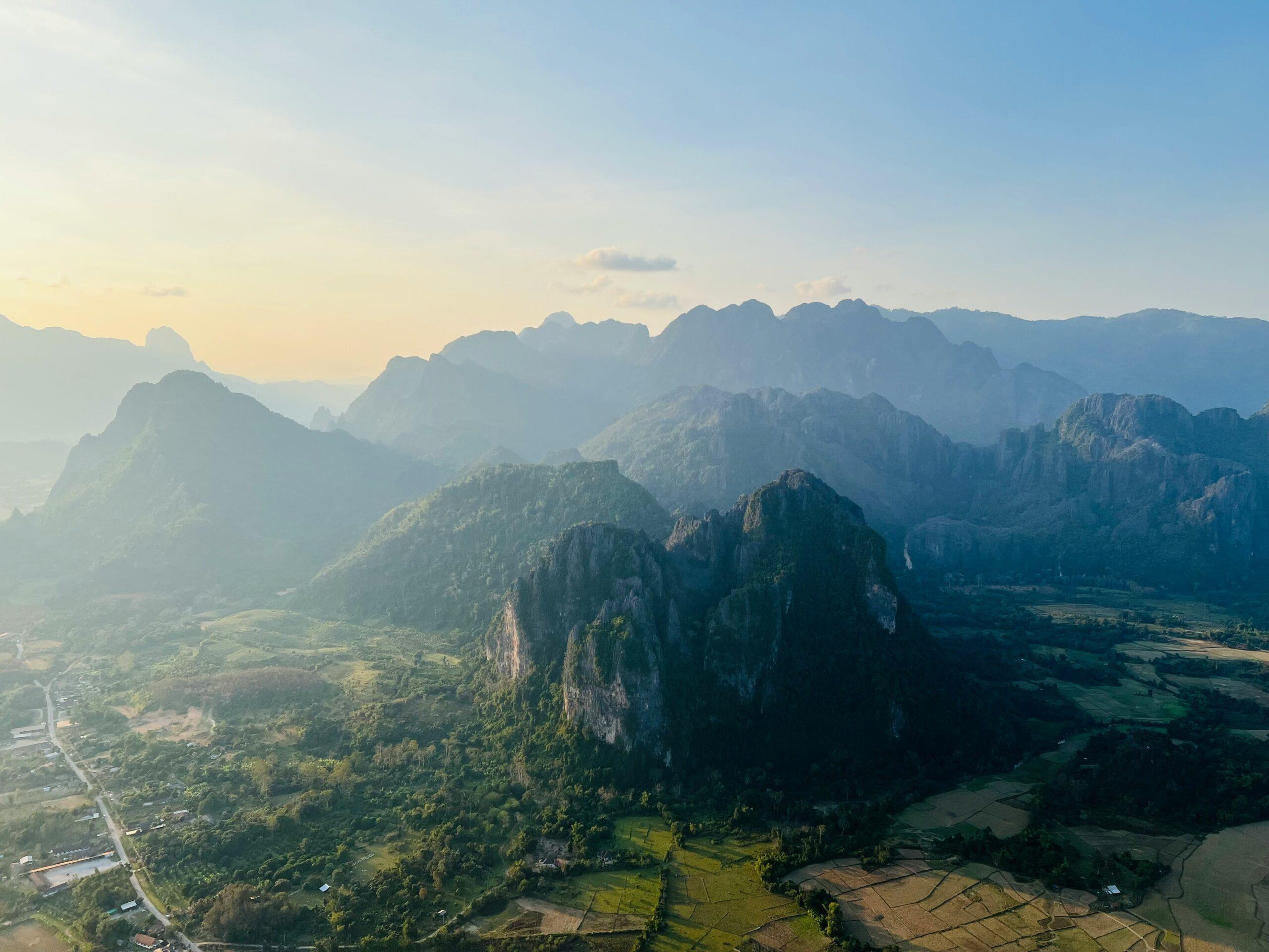 Vue aérienne d’une vallée montagneuse avec pics rocheux spectaculaires, forêts verdoyantes et champs en contrebas