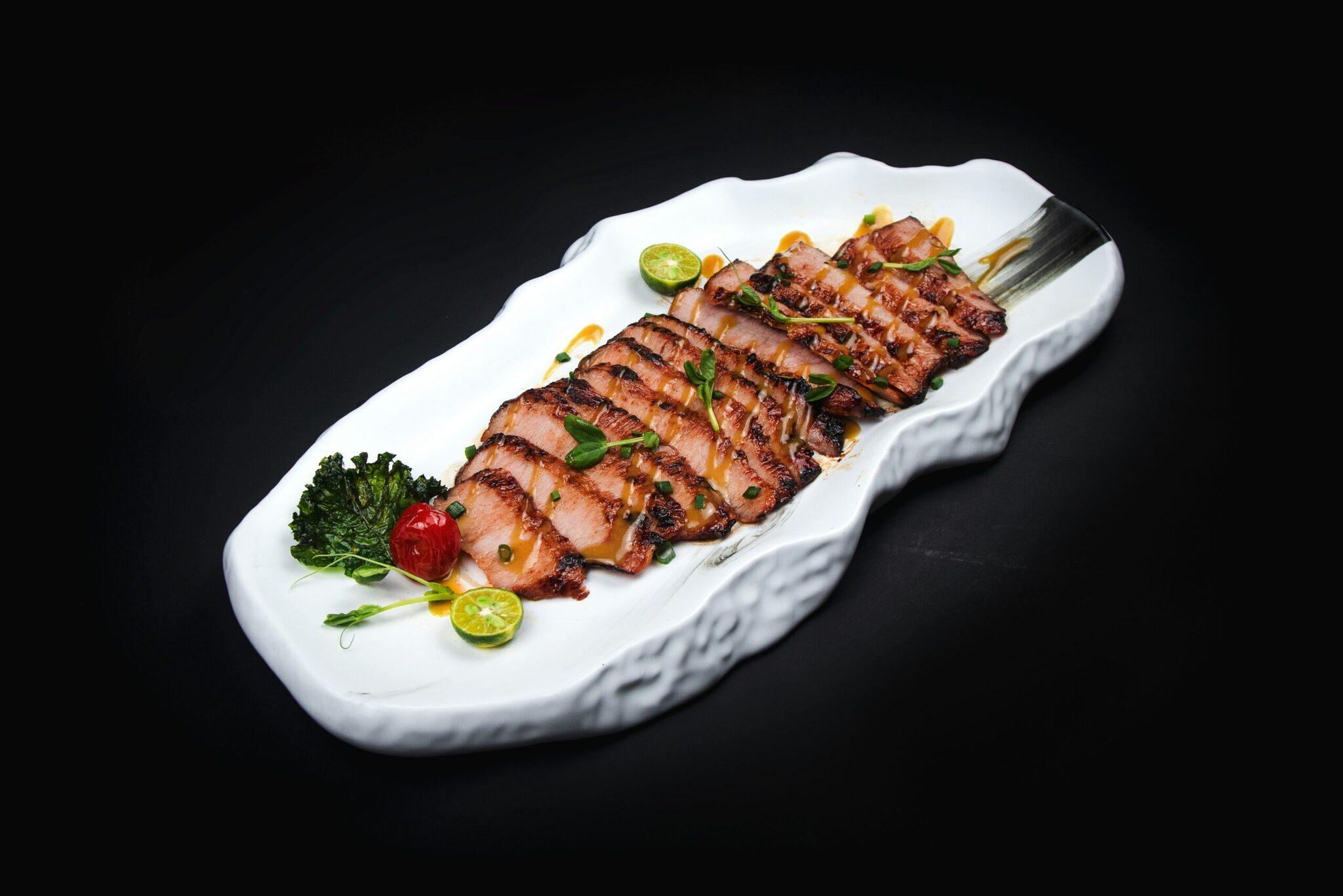 Canard laqué tranché finement présenté sur assiette blanche avec garnishes fraîches, spécialité culinaire asiatique
