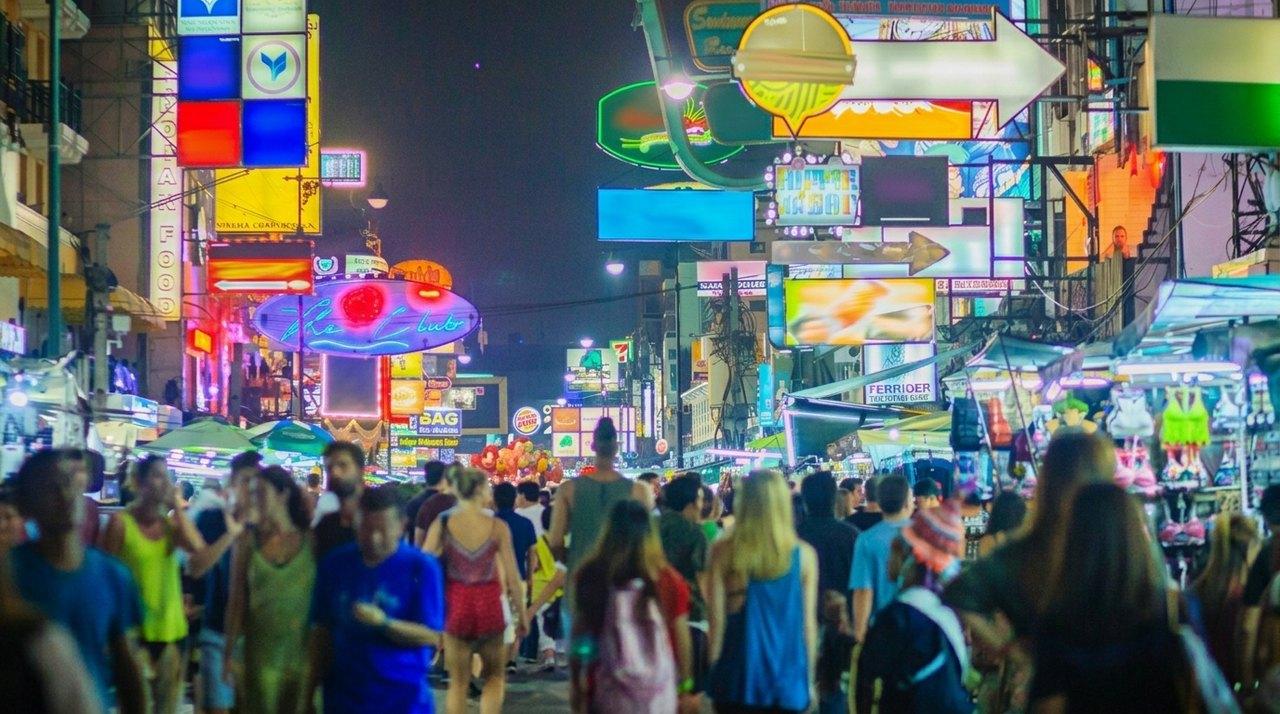 Une rue commerciale animée la nuit, illuminée par des enseignes colorées et remplie de foules de touristes et de passants