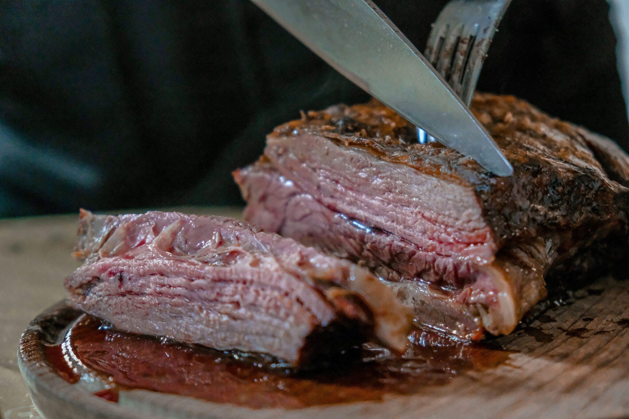 Un couteau coupe une tranche de viande rouge saignante sur une planche en bois, illustrant la gastronomie locale