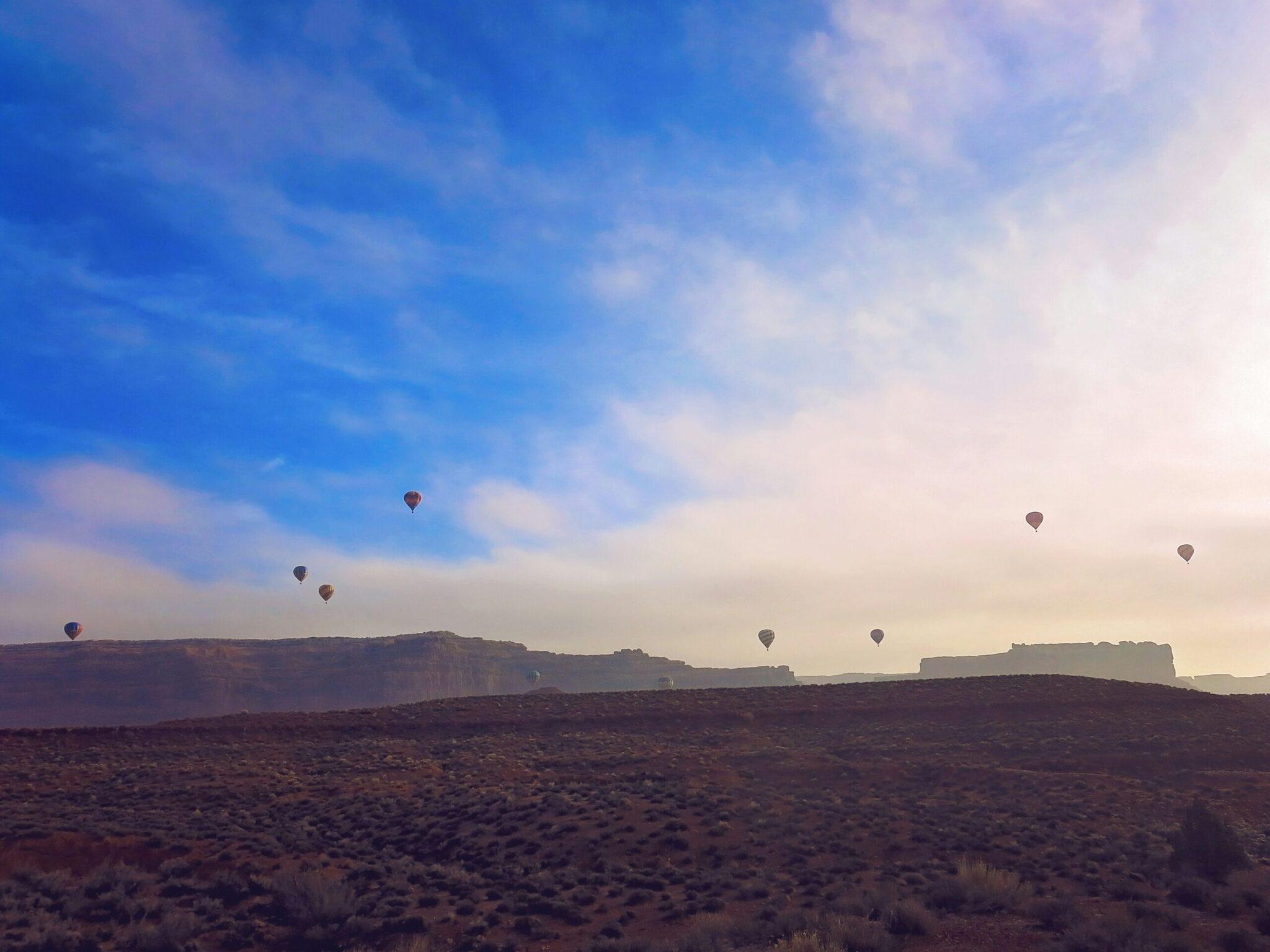 Plusieurs ballons colorés survolant un paysage désertique aride avec formations rocheuses en arrière-plan