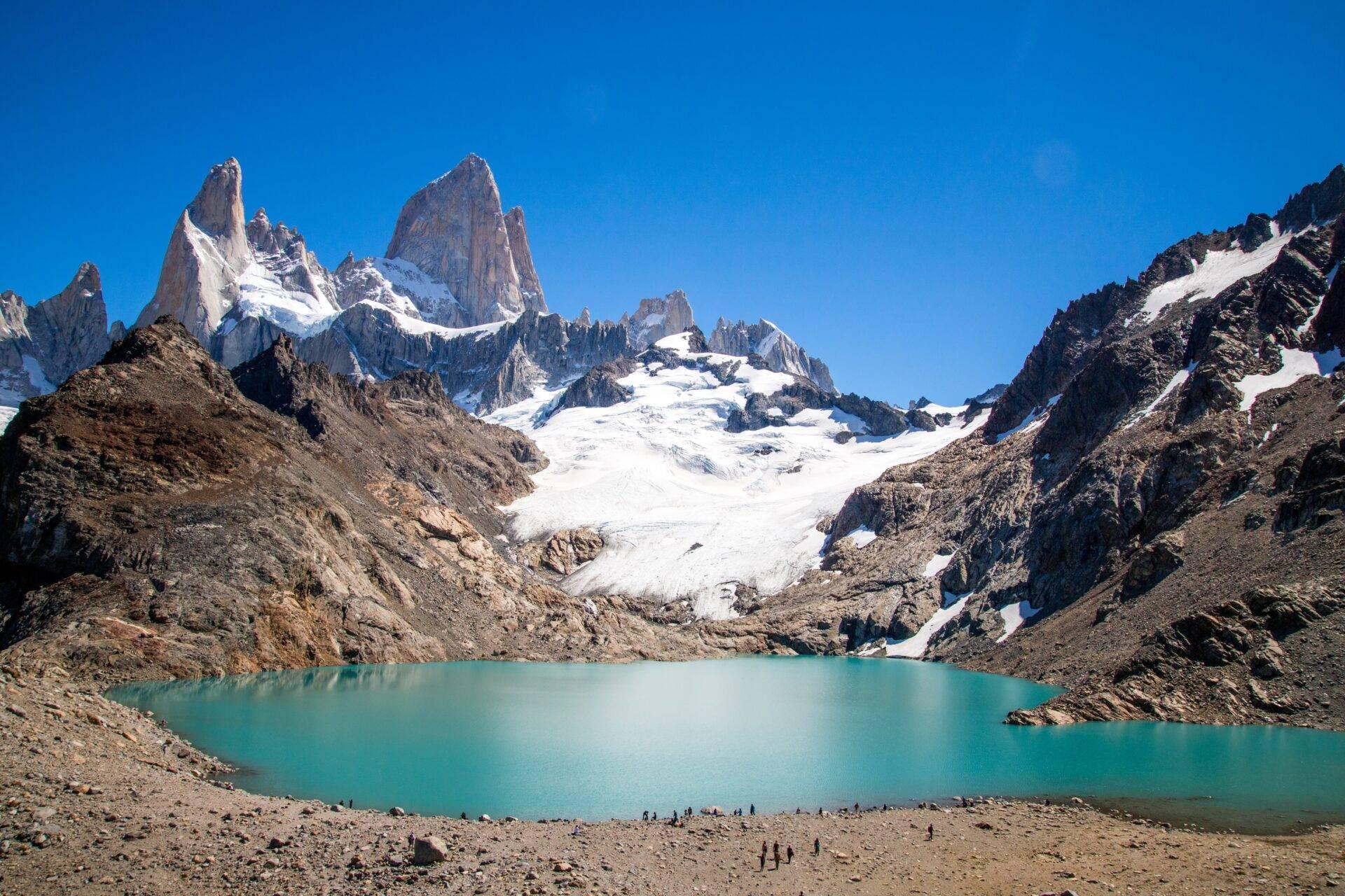 Lac turquoise glaciaire encadré par des pics rocheux enneigés et un glacier blanc sous ciel bleu dégagé
