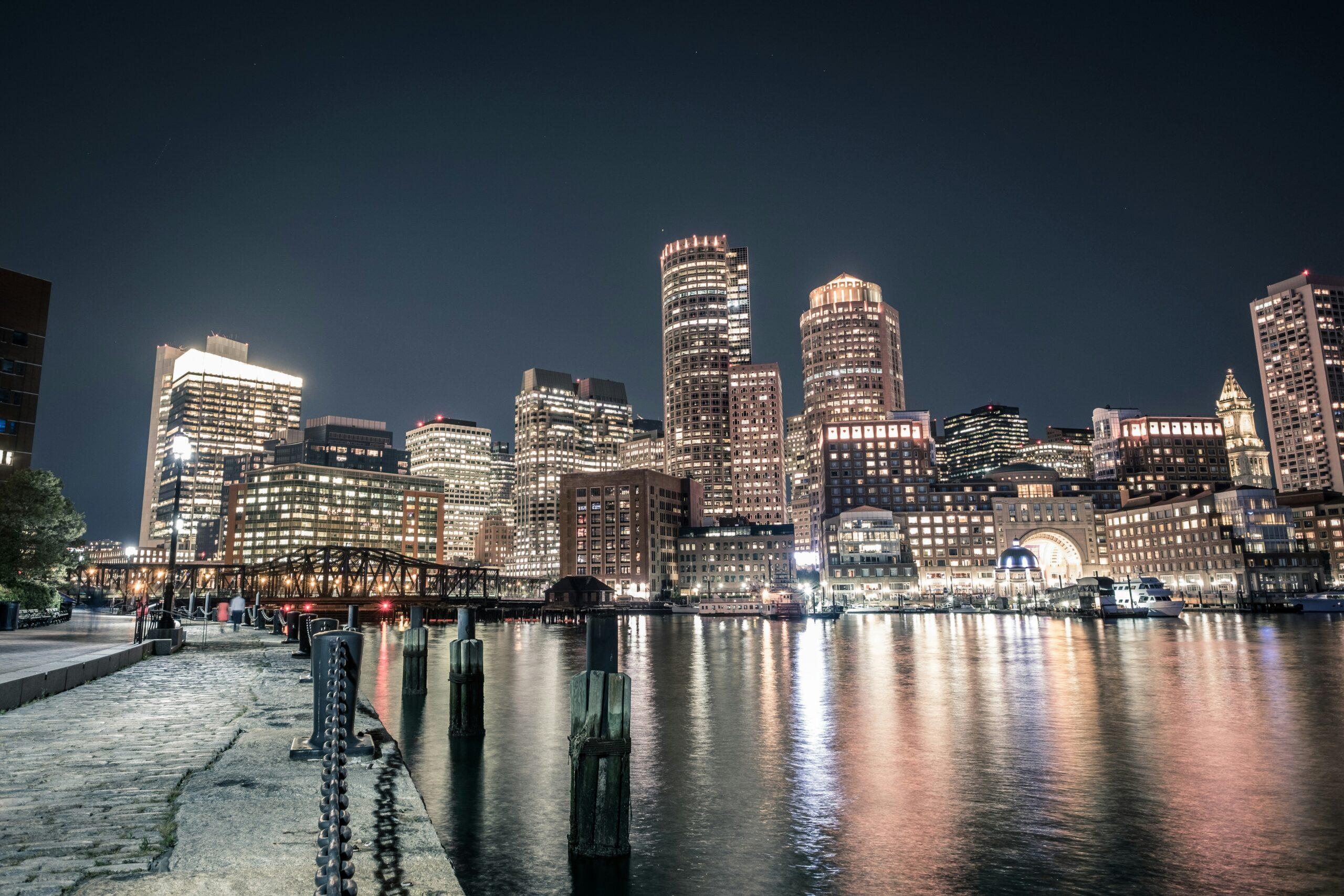 Skyline illuminé d’une grande ville côtière la nuit, avec gratte-ciel et pont métallique bordant une baie