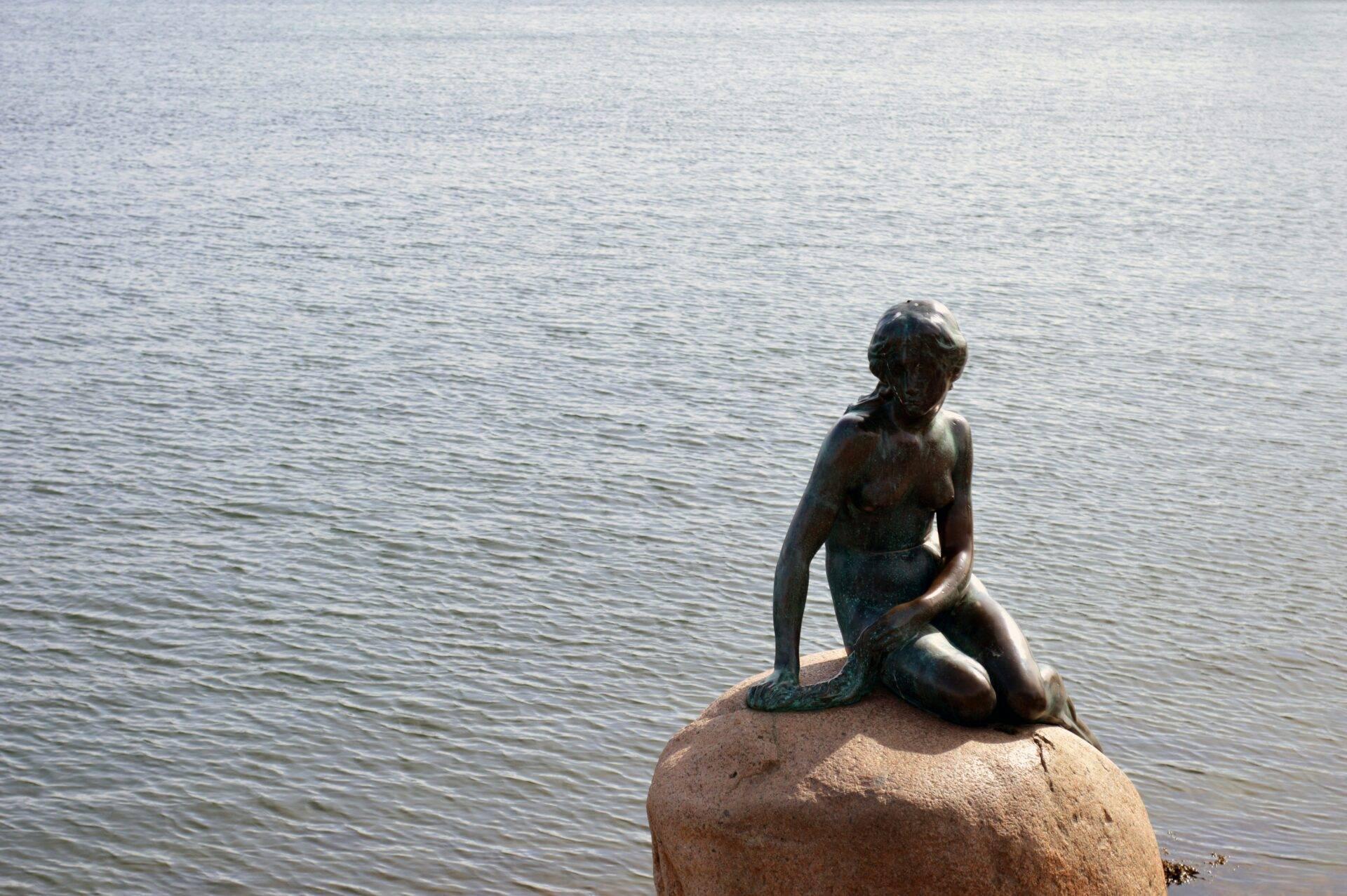 Statue de petite sirène assise sur un rocher face à la mer, célèbre monument touristique côtier