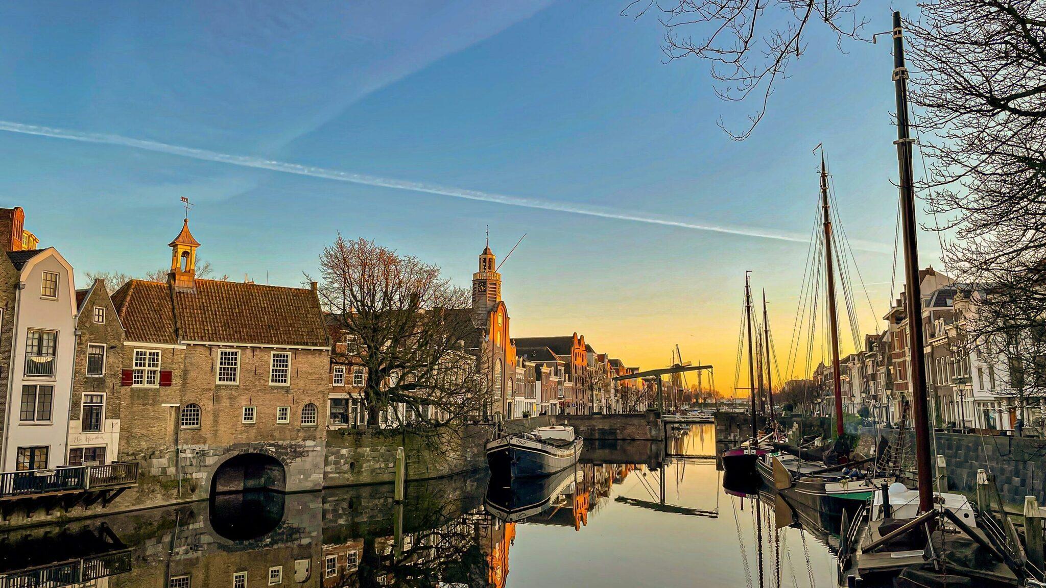 Canal historique avec maisons traditionnelles, voiliers amarrés et églises au coucher de soleil dans une ville portuaire néerlandaise
