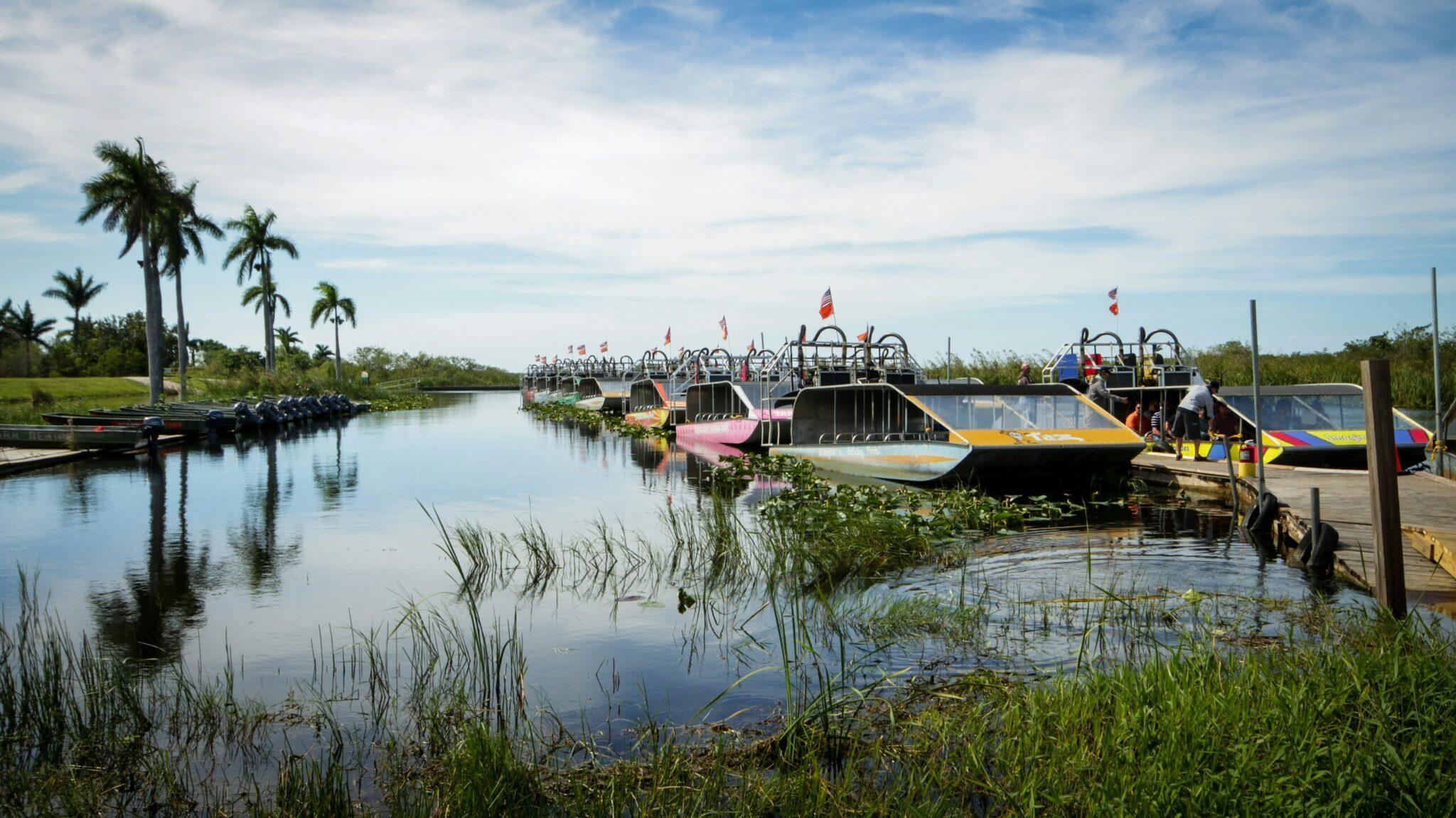 Des airboats colorés amarrés sur un canal des Everglades bordé de palétuviers et de végétation luxuriante