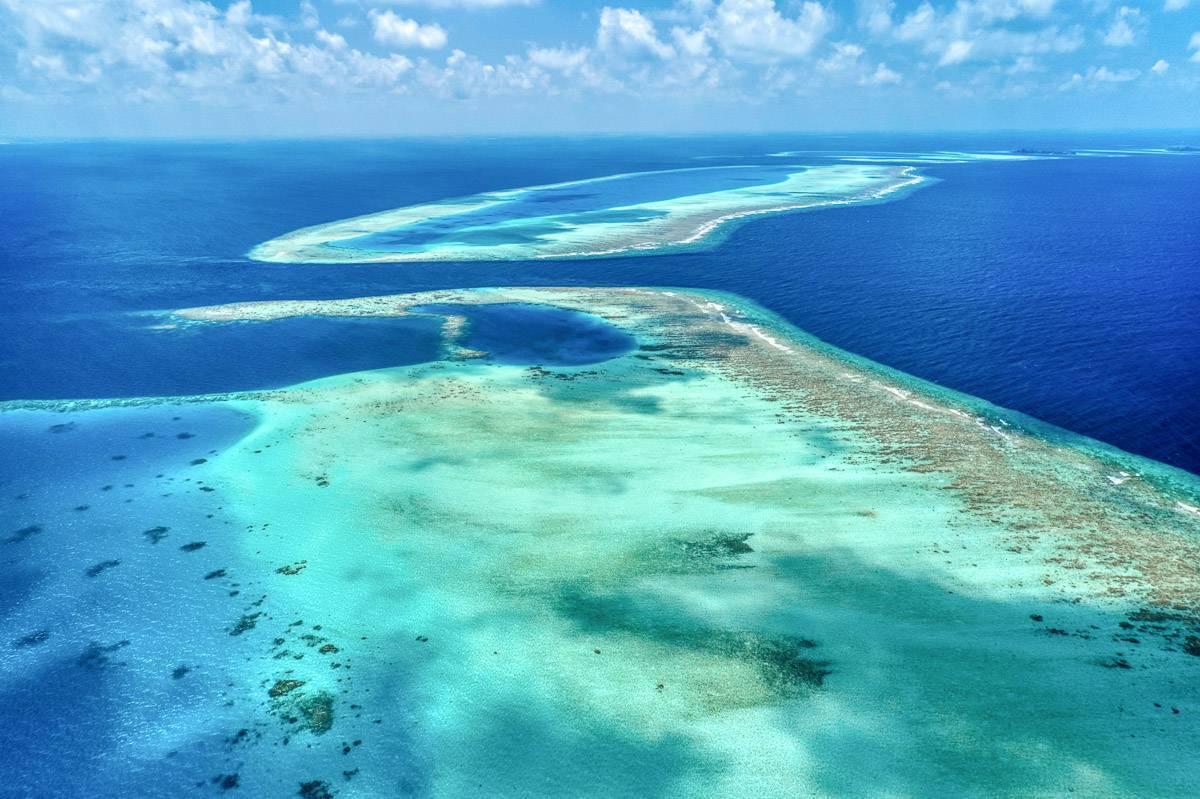 Vue aérienne d’atolls coralliens aux eaux turquoise et lagon bleu profond sous ciel dégagé