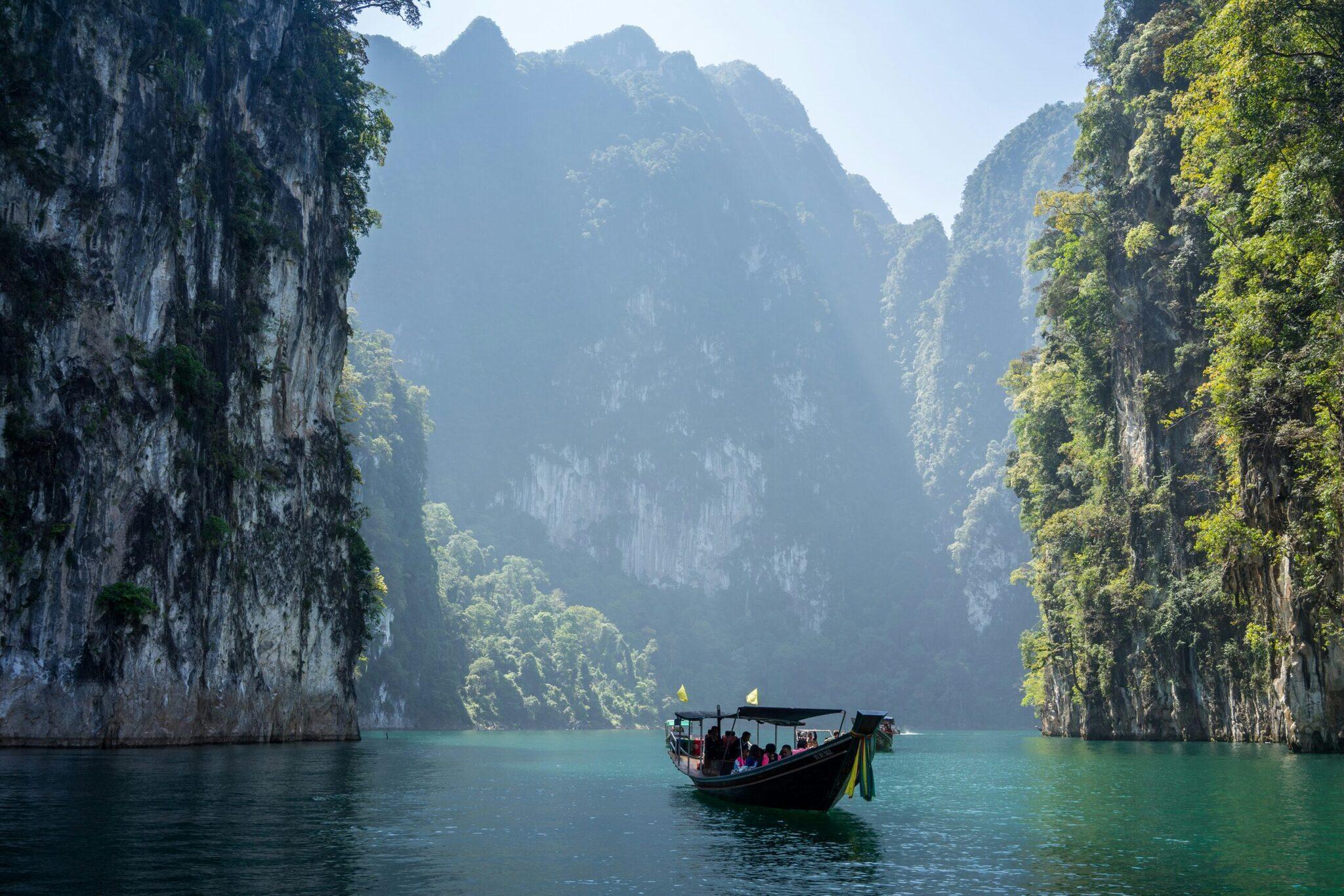 Un bateau traditionnel noir navigue dans une baie turquoise encadrée de falaises calcaires verticales couvertes de végétation