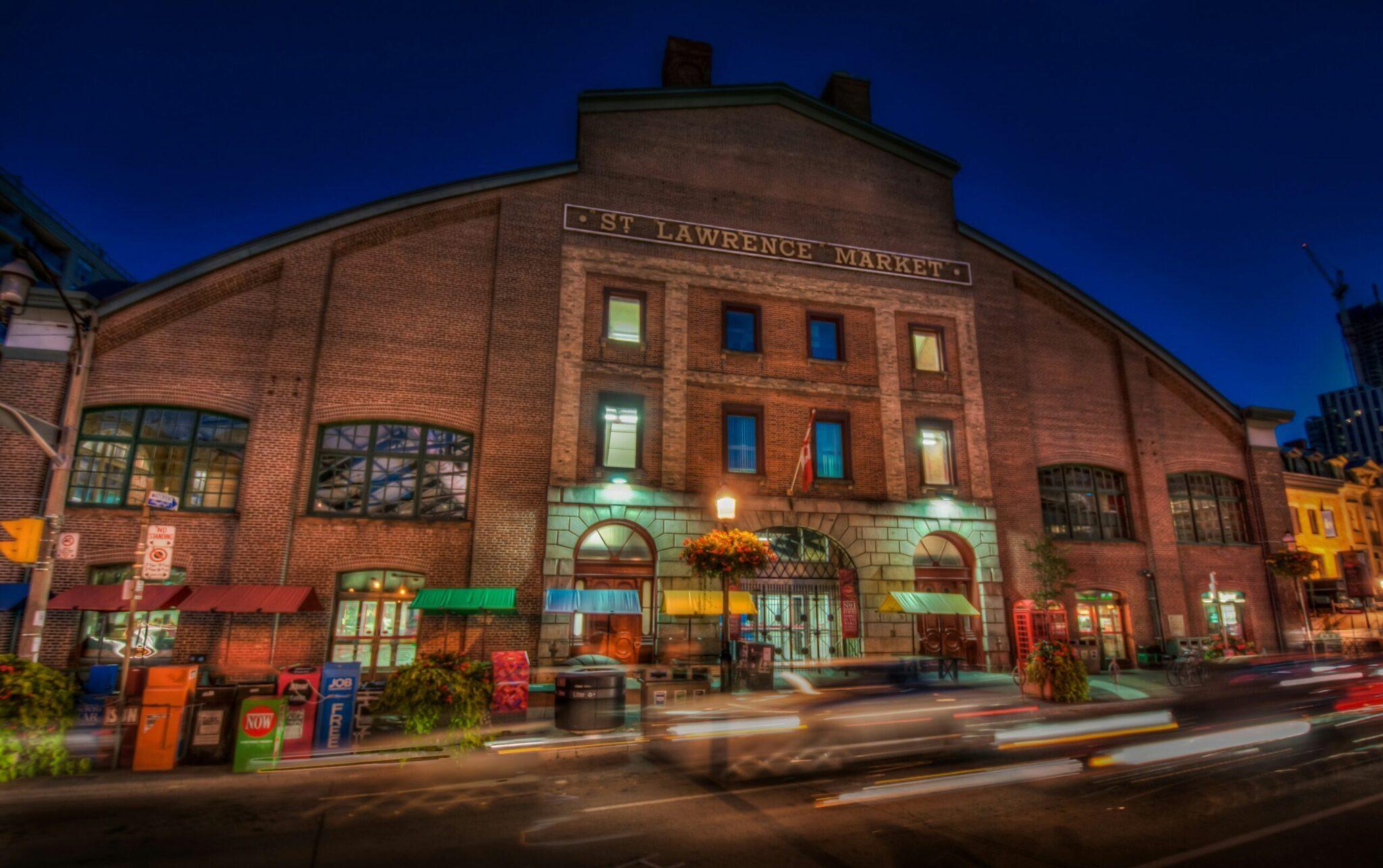 Le marché St Lawrence, bâtiment historique en brique rouge illuminé à la tombée du jour, avec commerces au rez-de-chaussée