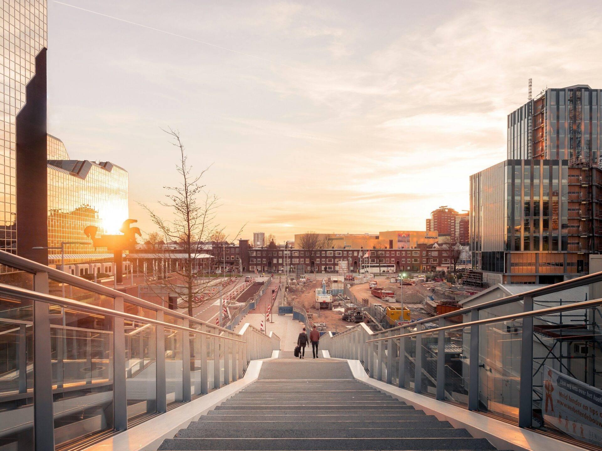 Vue depuis une passerelle moderne sur un chantier urbain en transformation avec bâtiments historiques et modernes au coucher de soleil