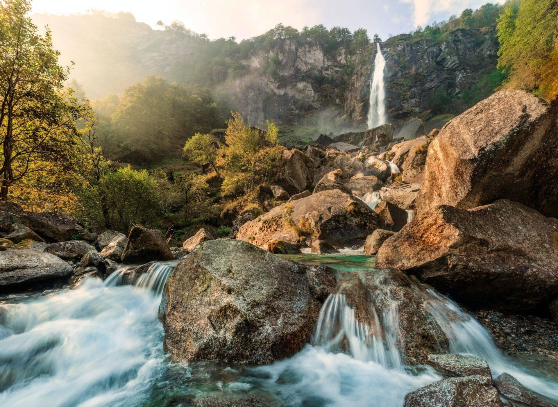 Cascade spectaculaire s’écoulant entre des falaises rocheuses dans une vallée verdoyante avec rivière en premier plan