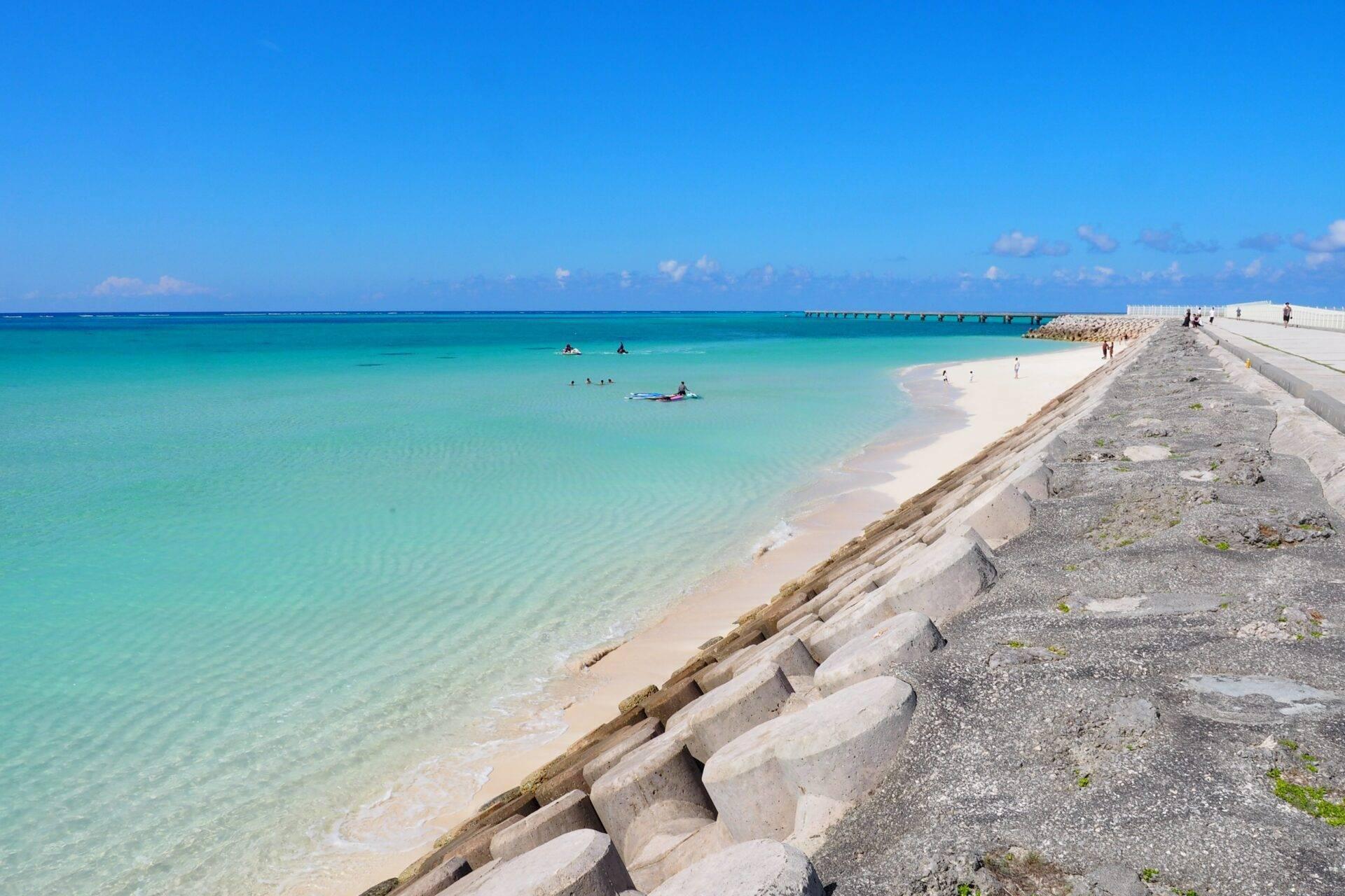 Une plage de sable blanc aux eaux turquoise cristallines avec digue en béton et baigneurs